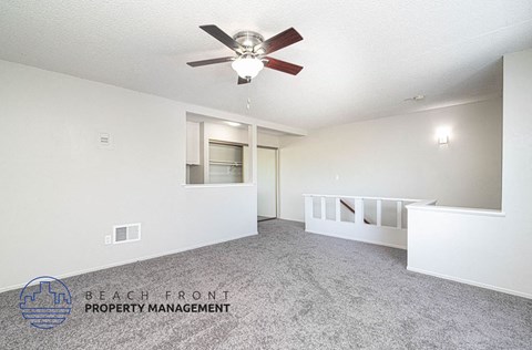 an empty living room with a ceiling fan and a staircase